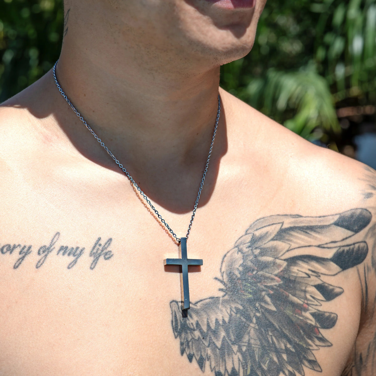 Silver cross pendant necklace worn over a tattooed chest.