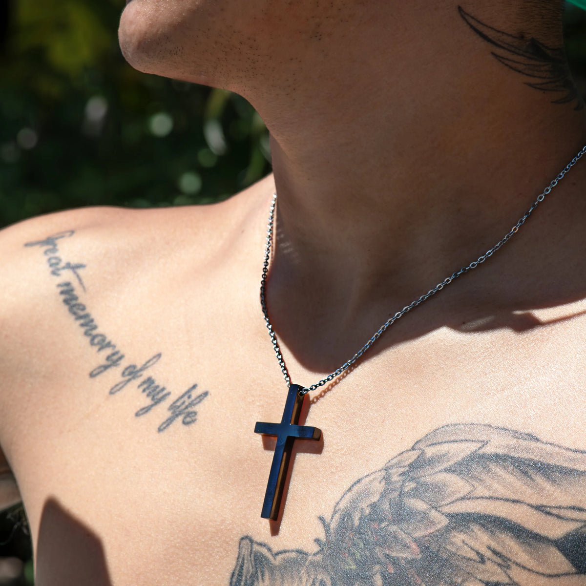Silver cross pendant necklace worn against tattooed skin.