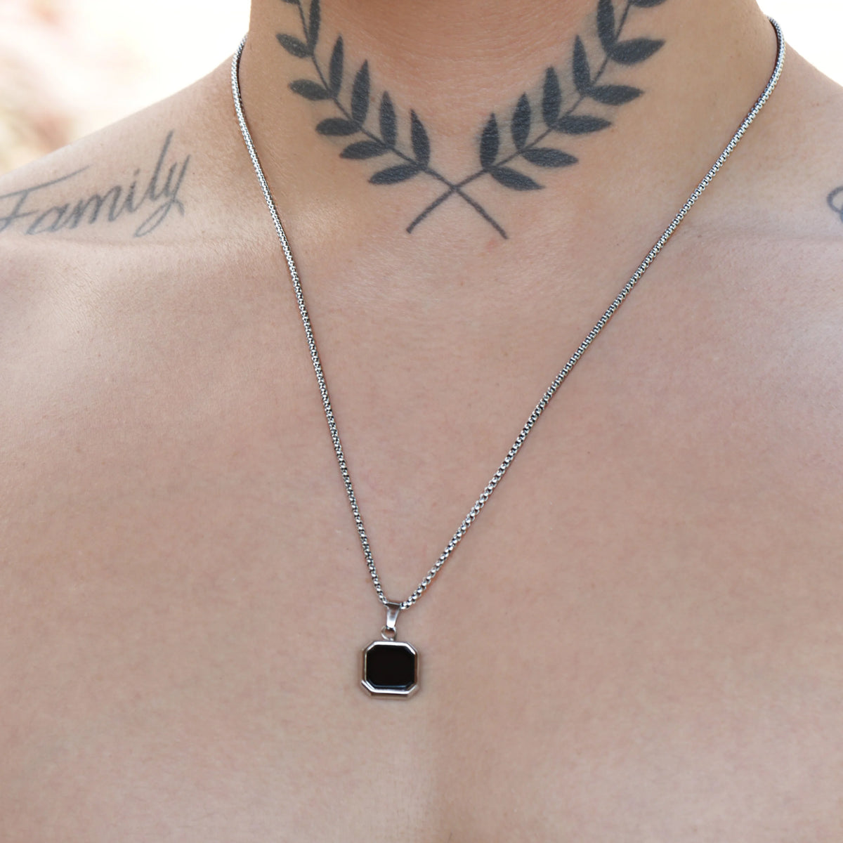 Silver chain necklace with a square black pendant.