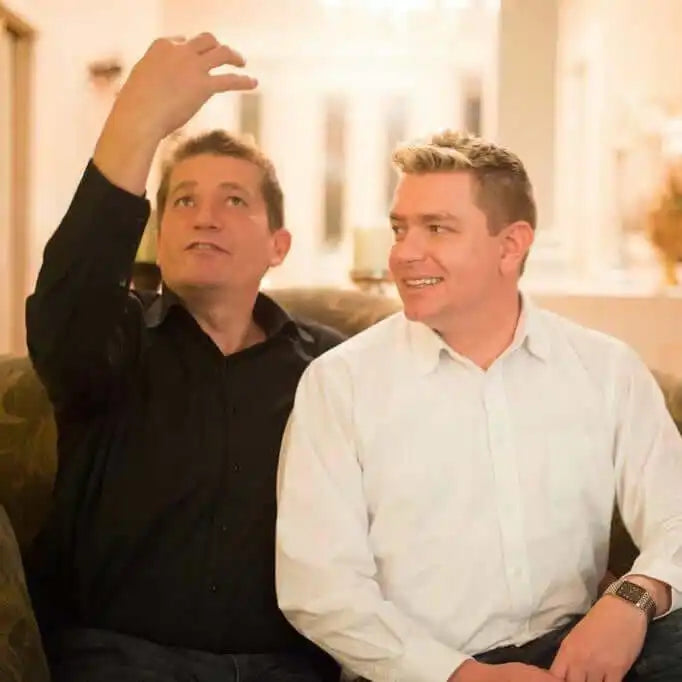 Two men sitting together, one wearing a black sweater and one in a white dress shirt.