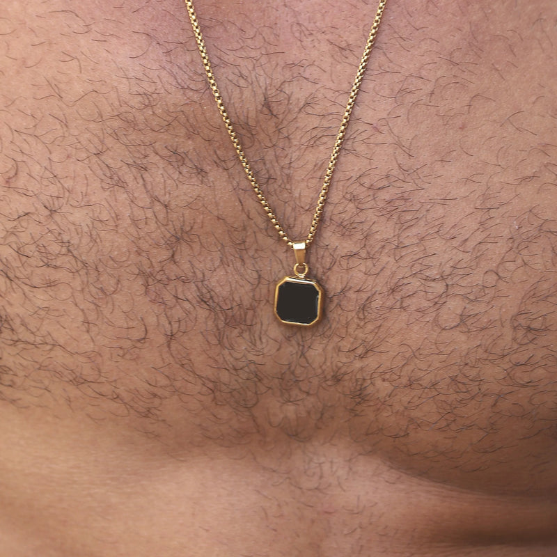 Gold necklace with a small square black pendant.