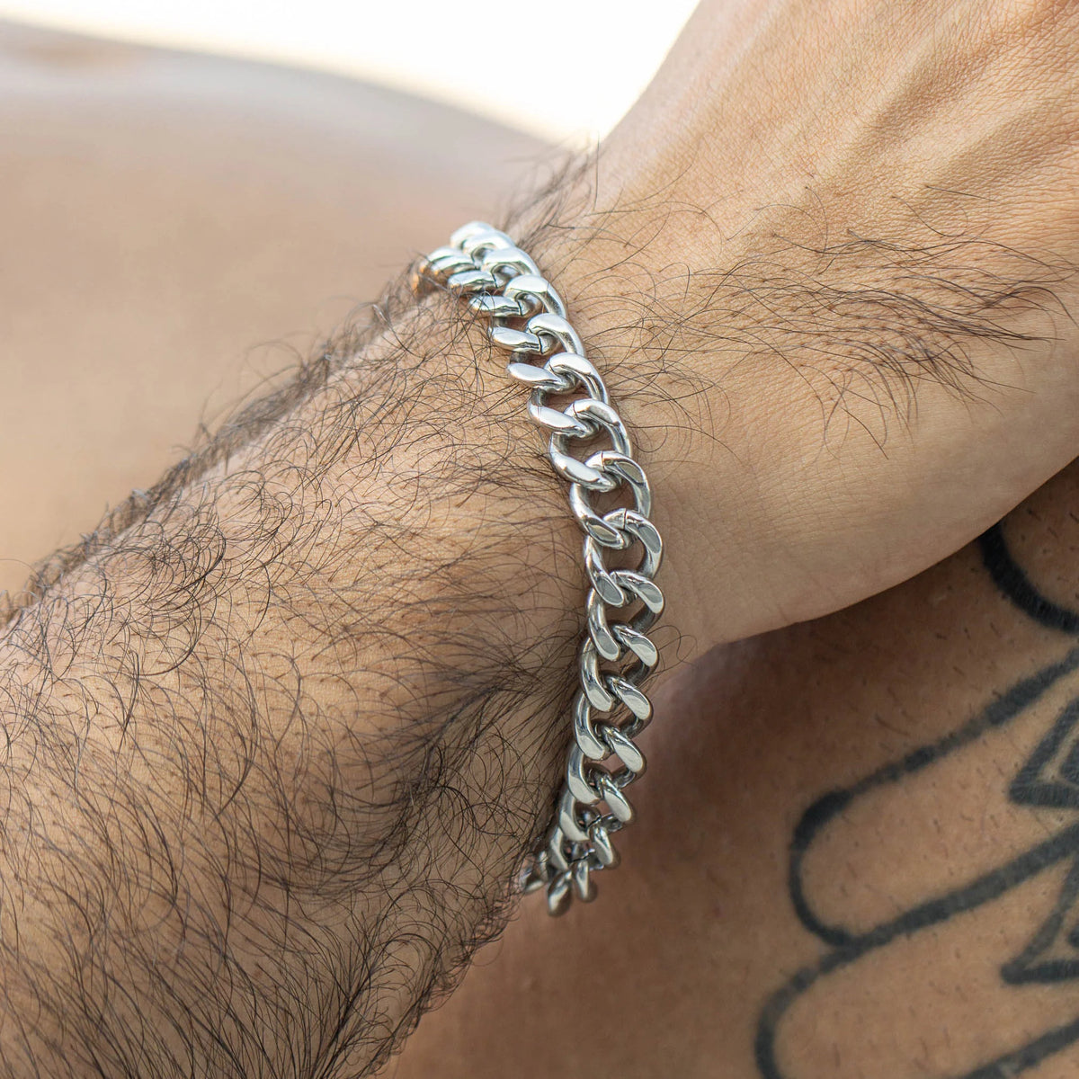 Silver chain-link bracelet worn on a tattooed wrist.