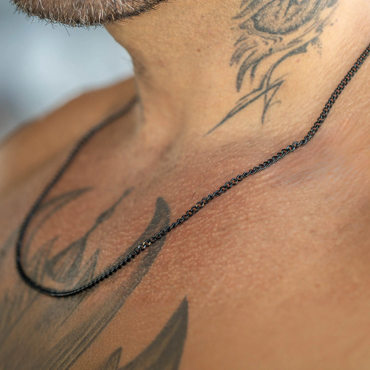 Simple black beaded necklace chain against tattooed skin.