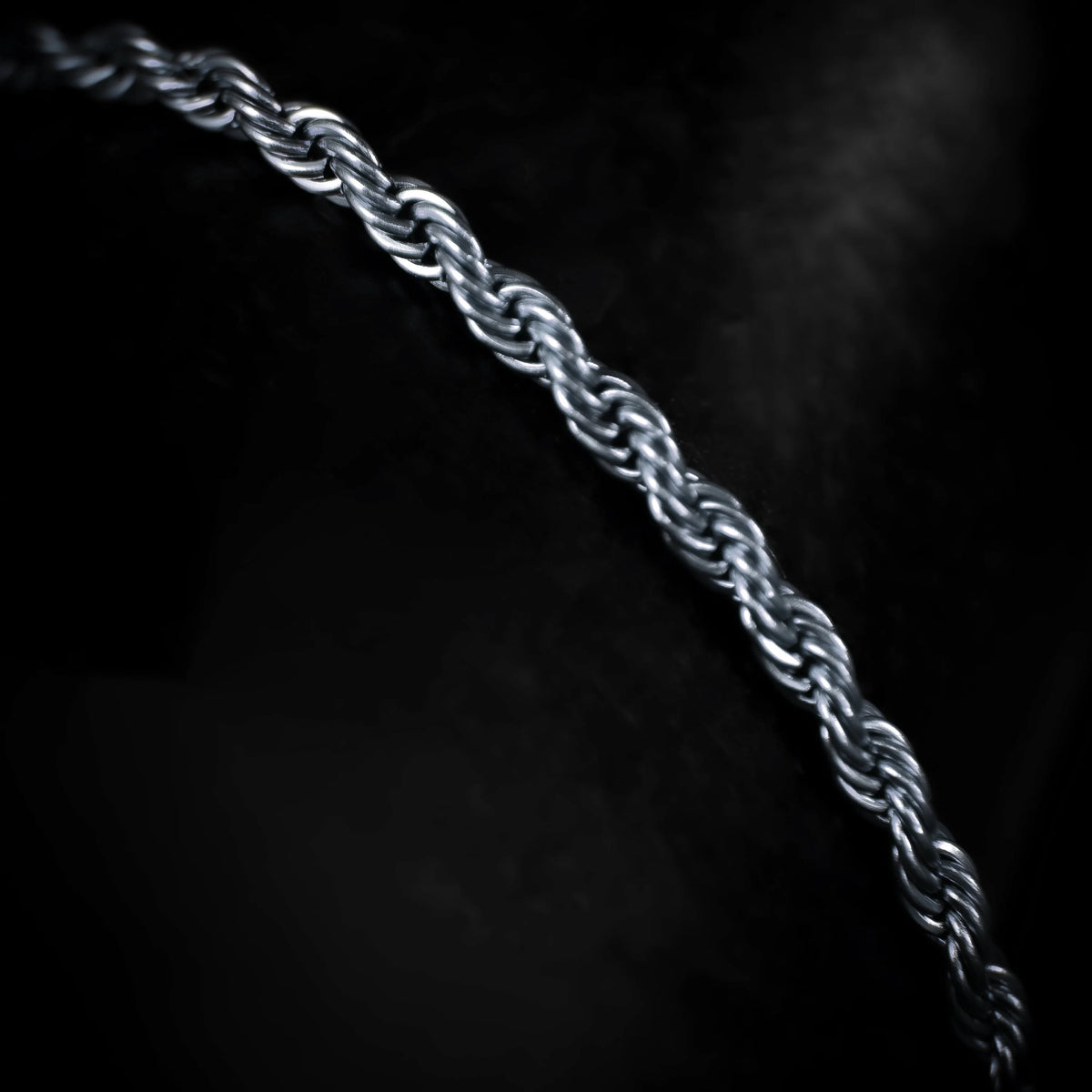 Silver twisted rope chain against a dark background.