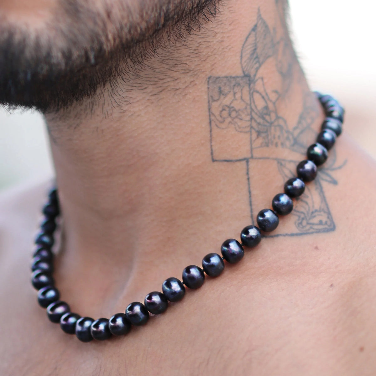 Black pearl necklace worn around a person’s neck with a visible tattoo nearby.