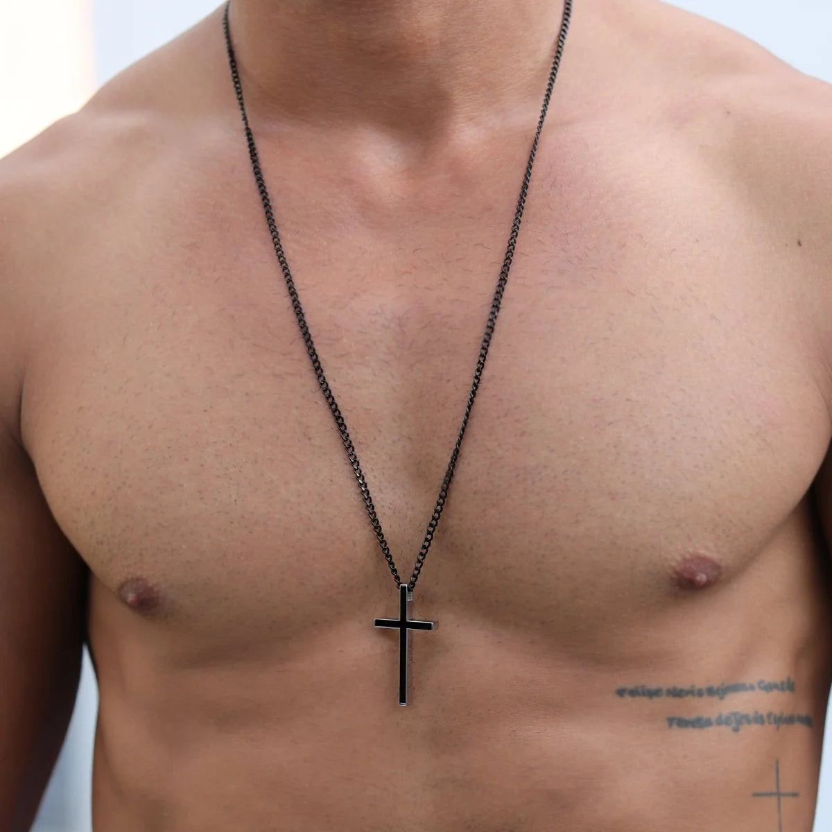 Black cross pendant necklace worn on a bare chest.