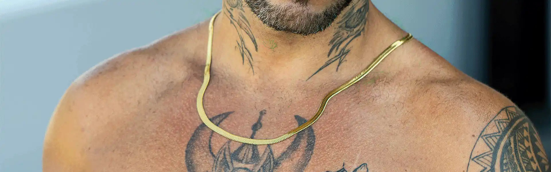 A bare-chested man with numerous tattoos and a gold snake chain necklace.