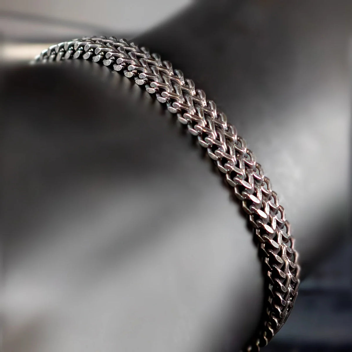 Intricately woven silver chain bracelet with a curved shape.