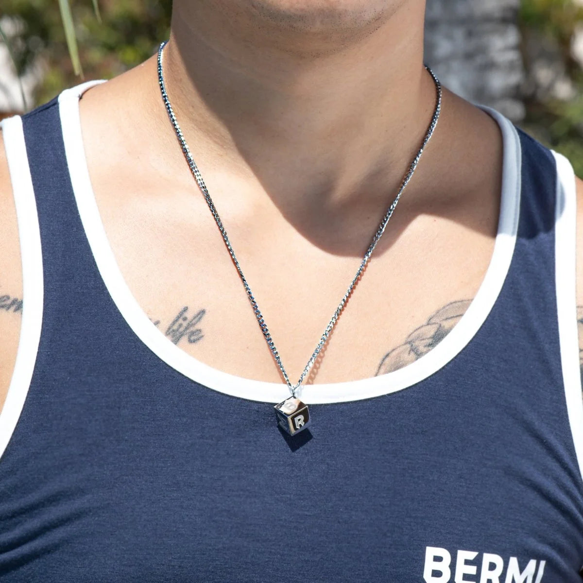 Silver necklace with a cube-shaped pendant worn over a navy blue tank top.