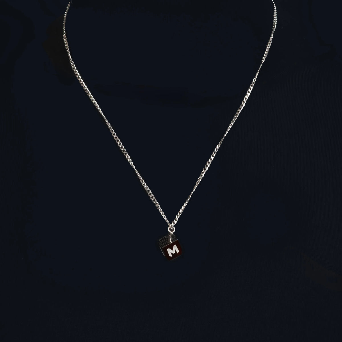 Silver necklace with a pendant featuring the letter ’M’.