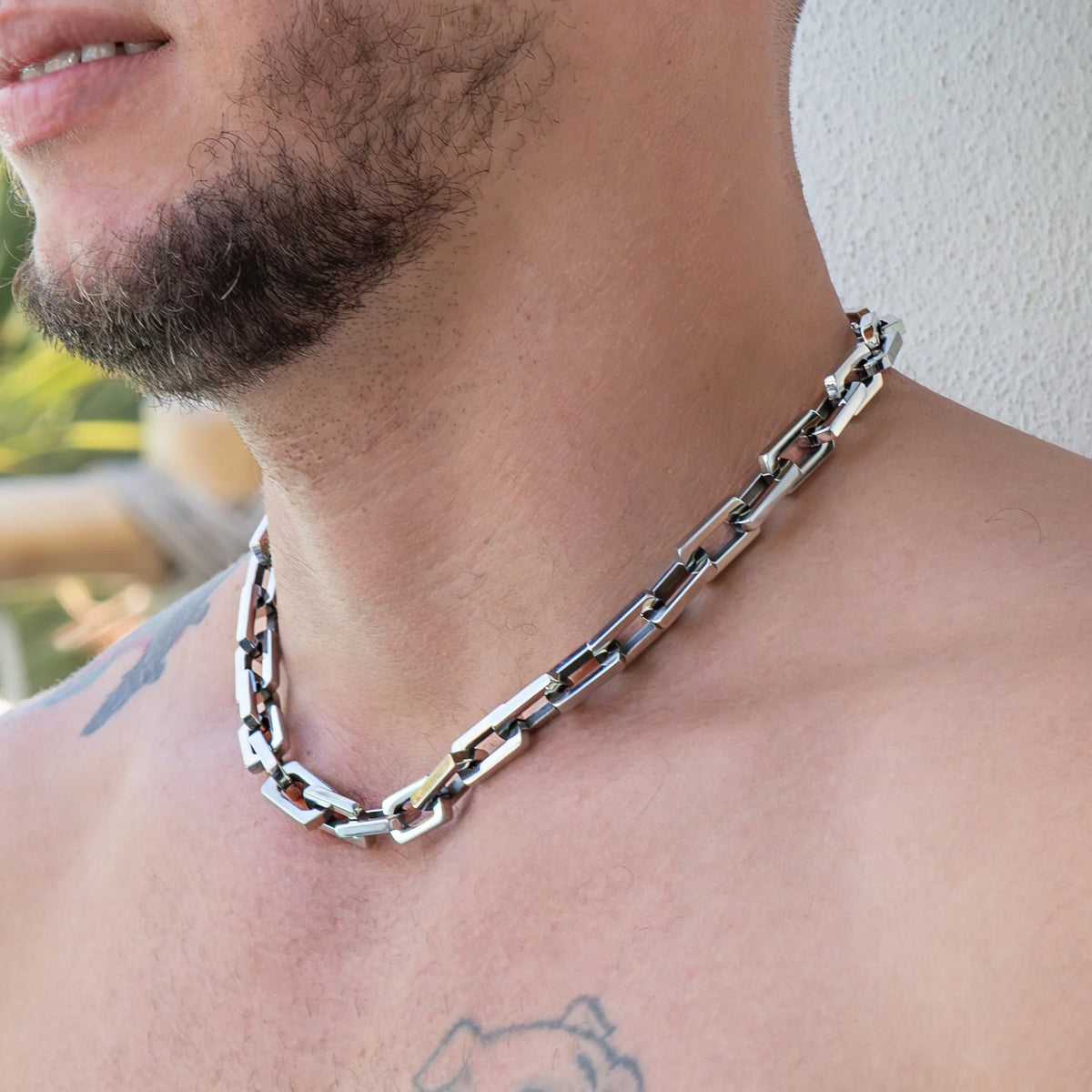 Silver chain necklace with rectangular links worn around a neck.