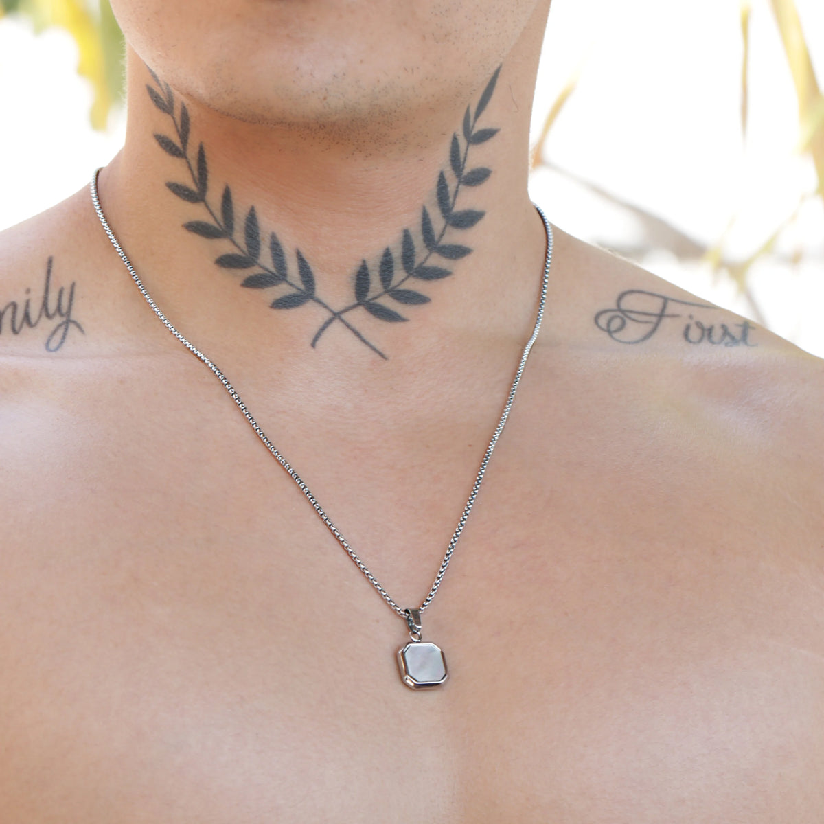 Laurel wreath tattoo on a neck with a silver necklace below it.