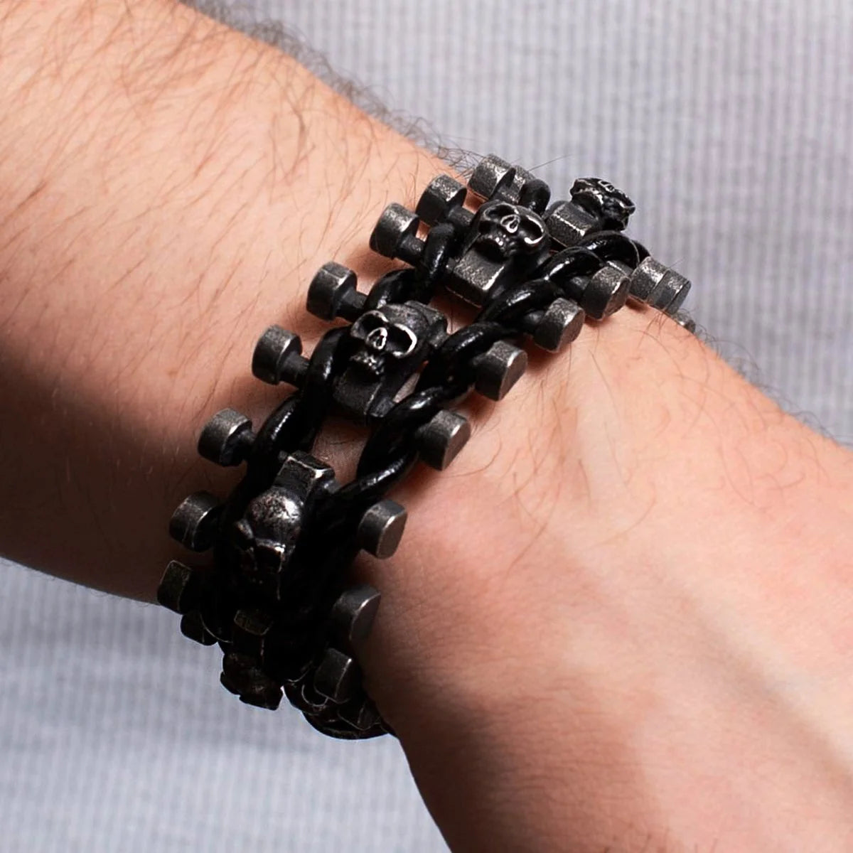 Black metal bracelet with skull designs and chain-like links worn on a wrist.