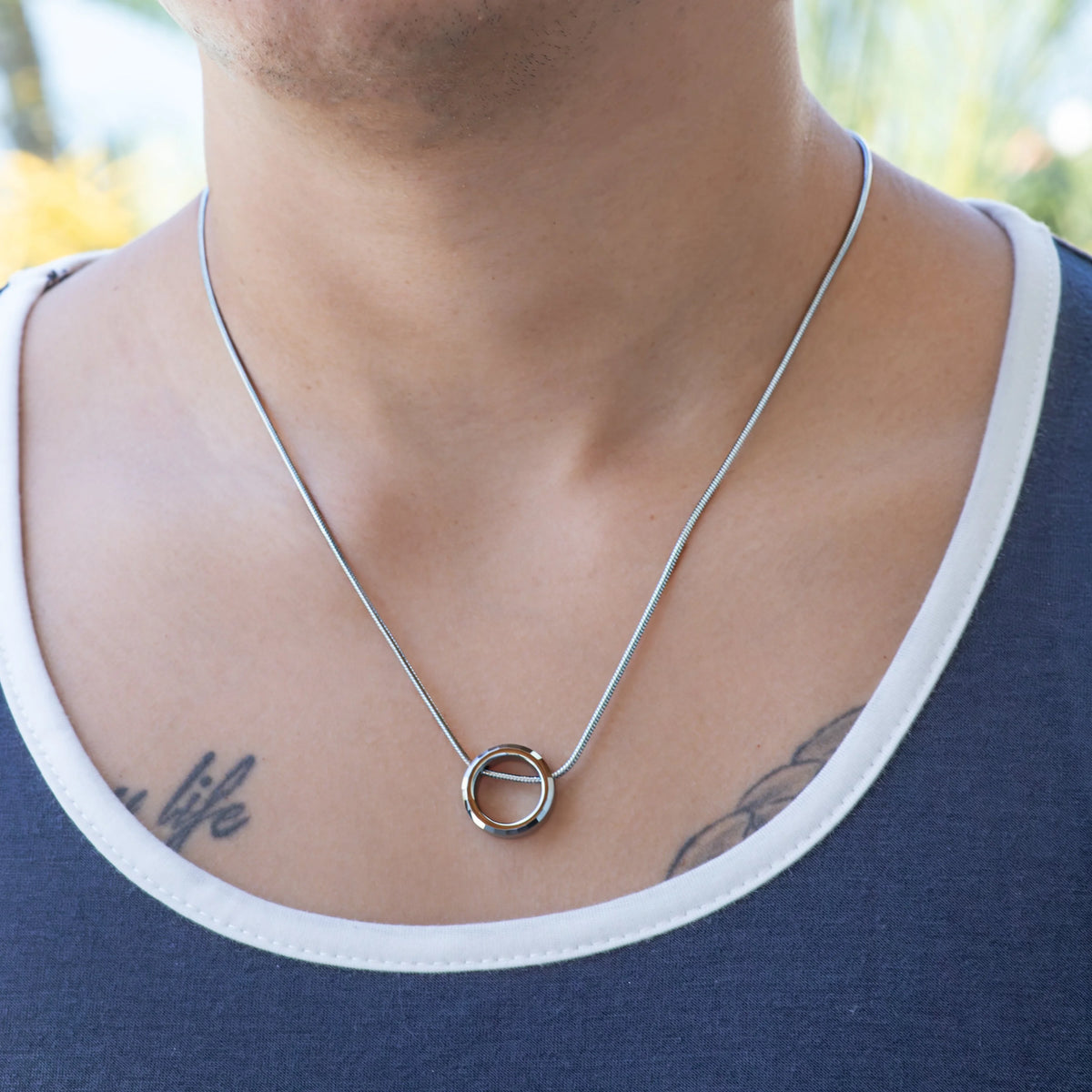 Simple silver necklace with a circular pendant worn around a person’s neck.