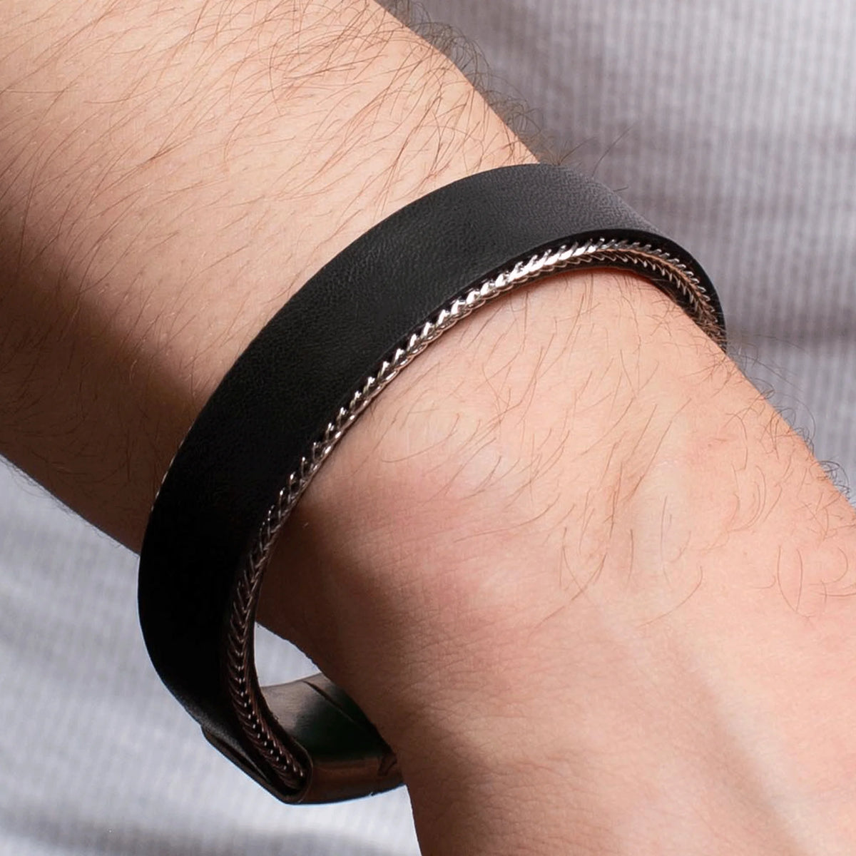 Black leather bracelet with a silver chain edge worn on a wrist.