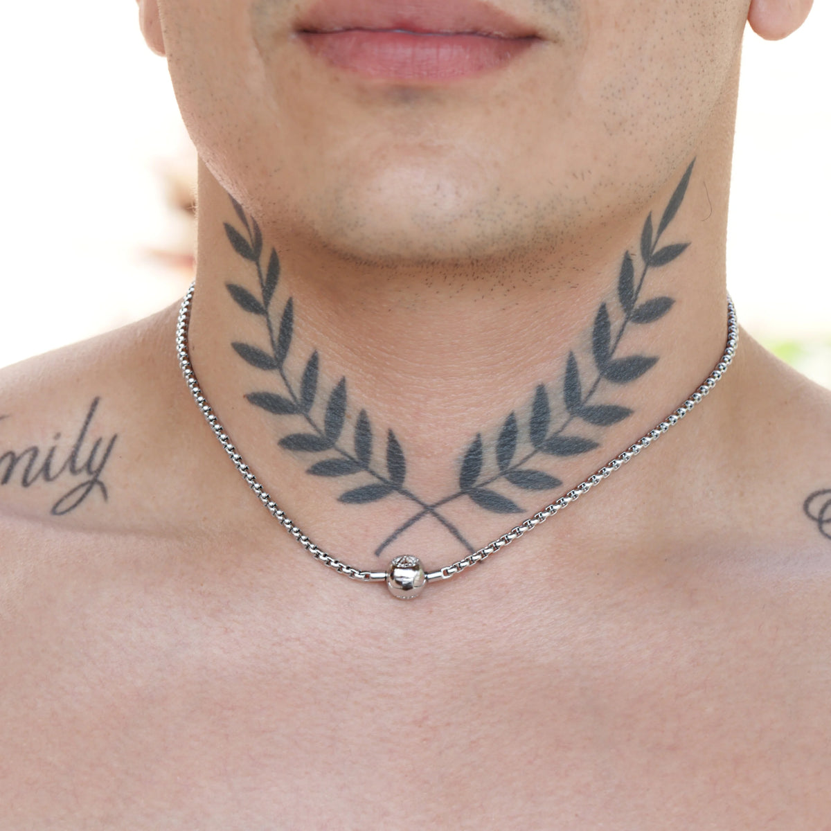 Tattoo of laurel wreath branches on a person’s neck, with a silver necklace visible.