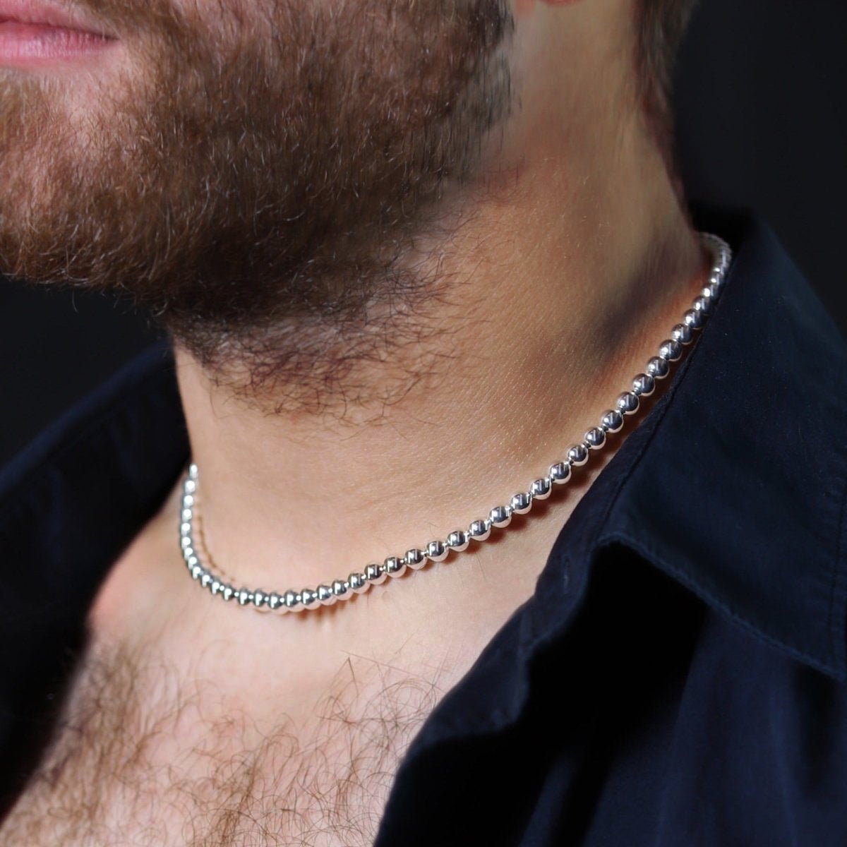 Silver beaded necklace worn around a person’s neck.