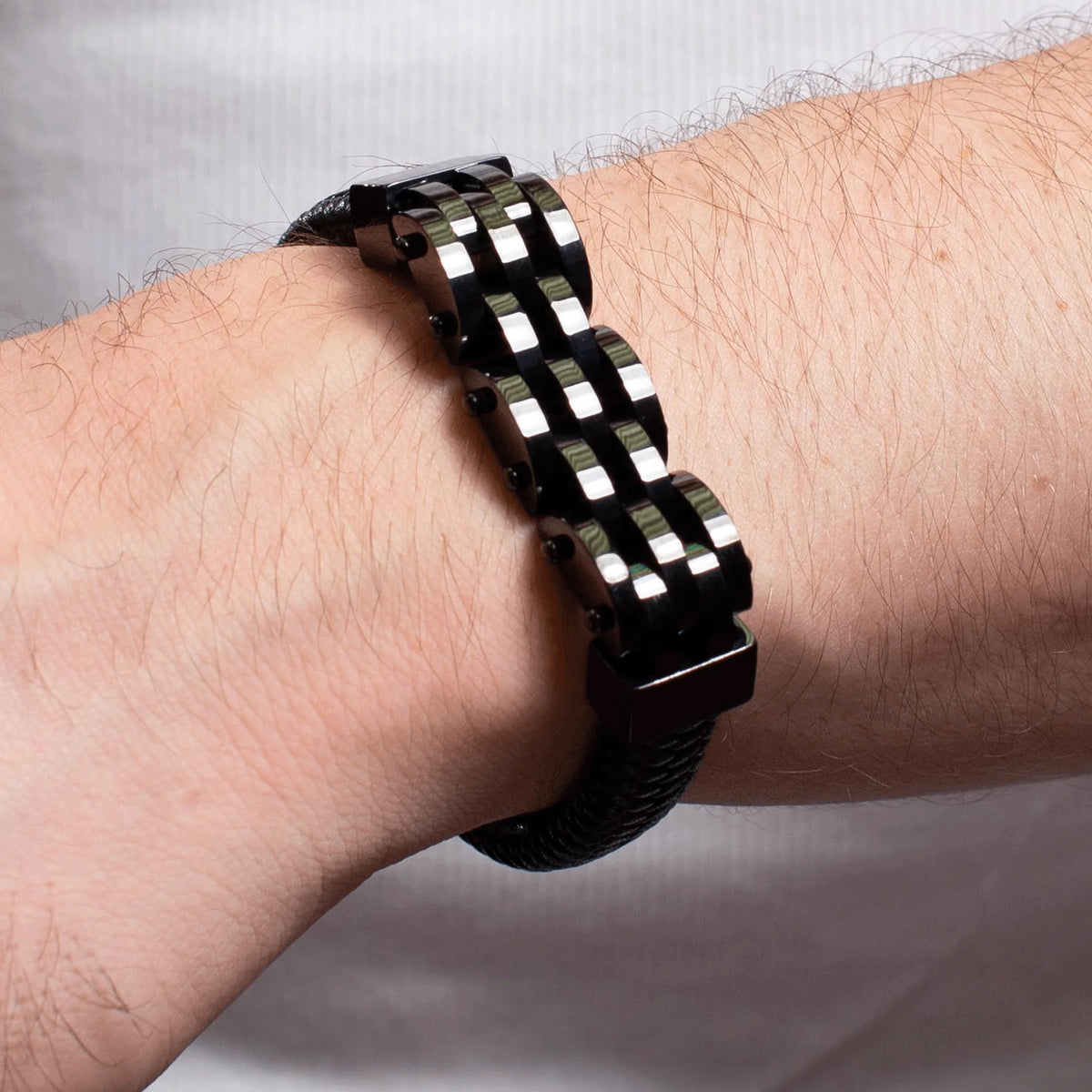 Checkered black and silver metal bracelet worn on a hairy wrist.