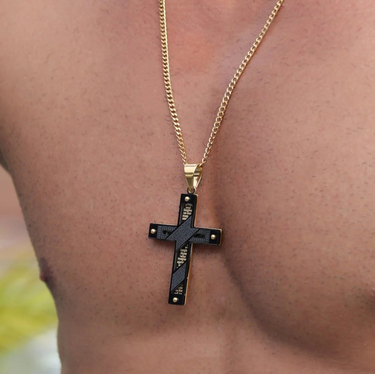 Gold chain necklace with a black cross pendant.