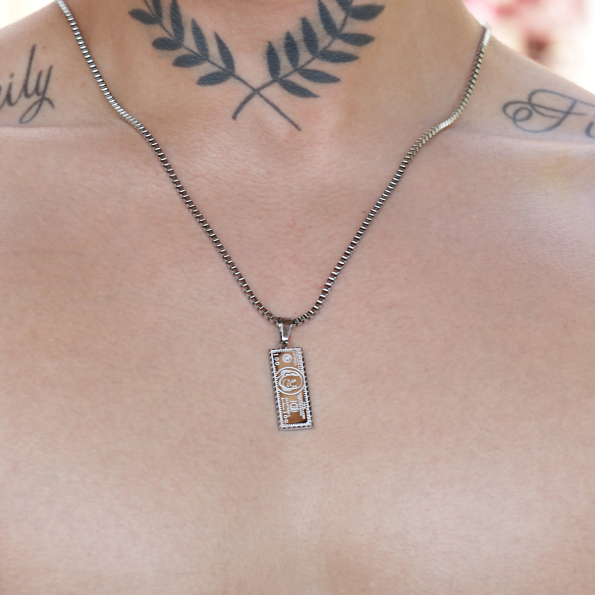 Rectangular pendant necklace with a dollar bill design hanging on a chain.