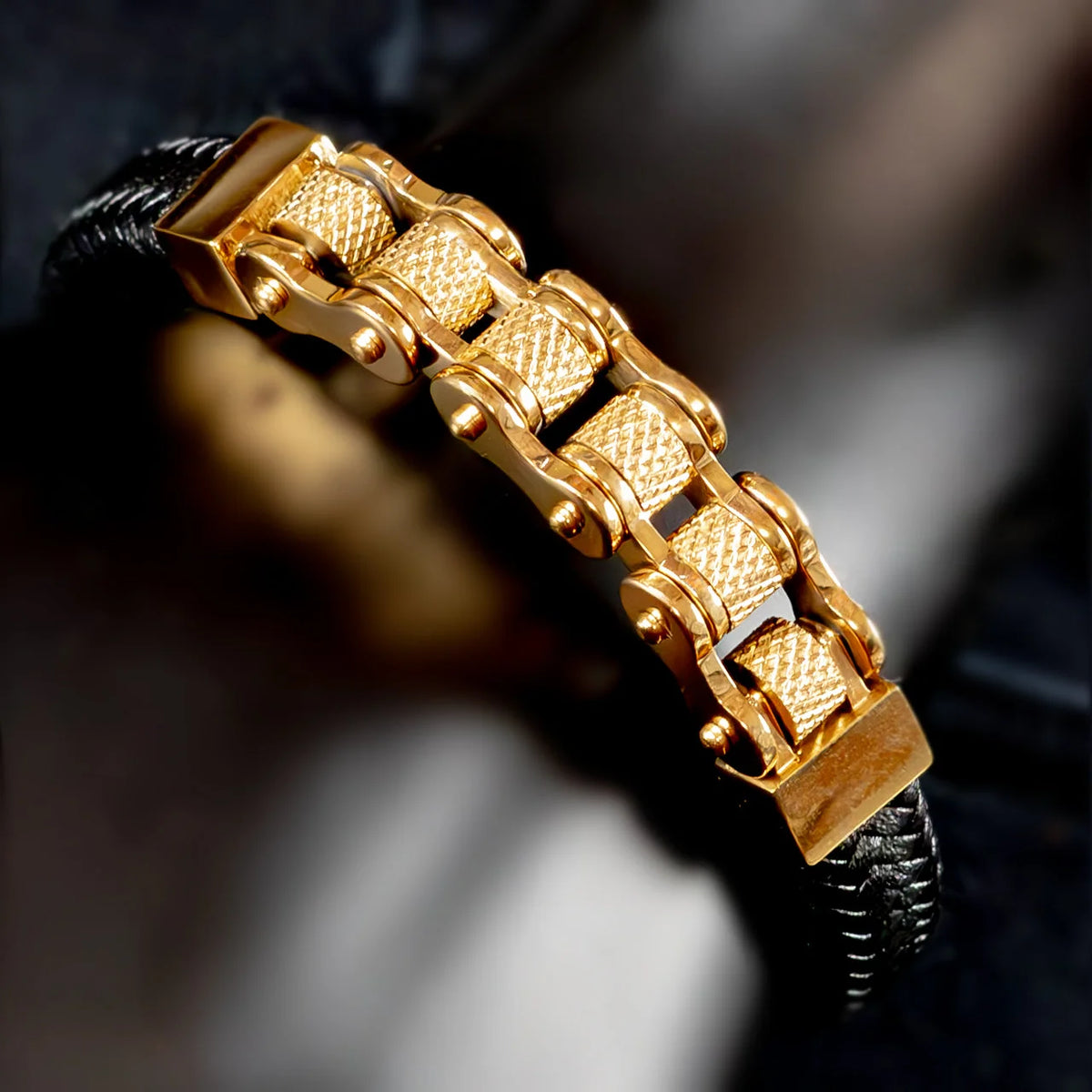 Gold-plated bracelet with intricate chain-link design on a black cord.