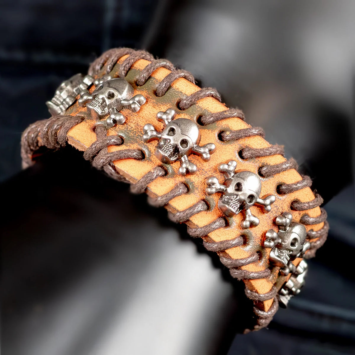 Leather bracelet adorned with silver skull and crossbones charms.