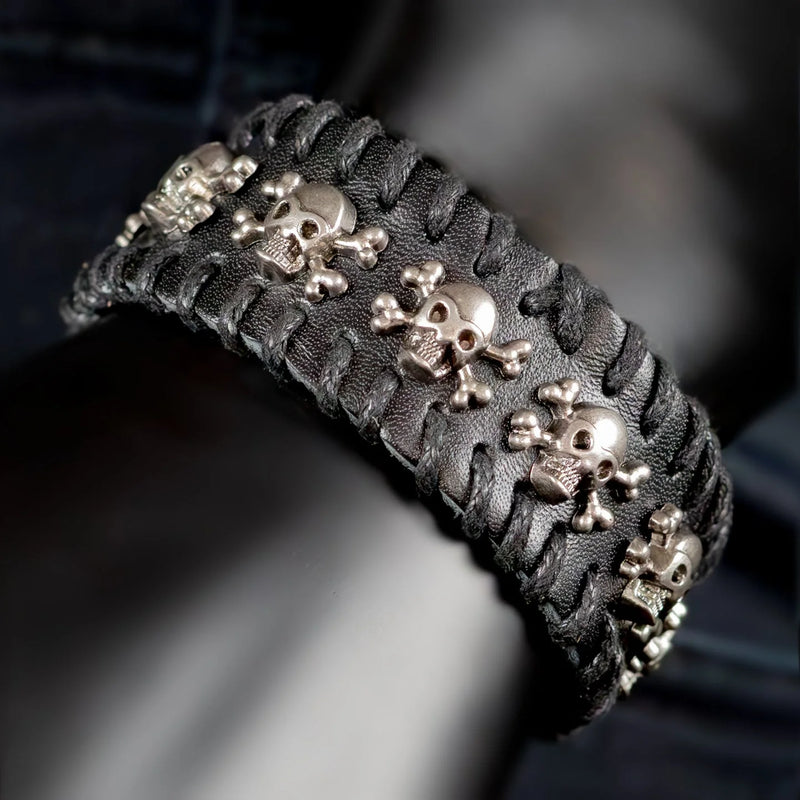 Leather bracelet adorned with metallic skull and crossbones charms.