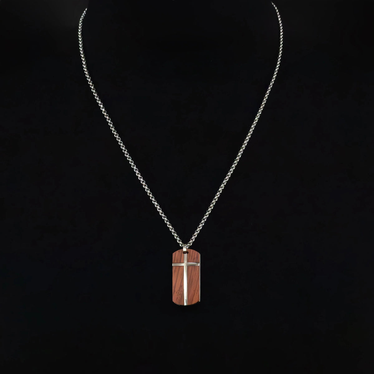 Wooden pendant with a metal cross inlay hanging from a silver chain necklace.