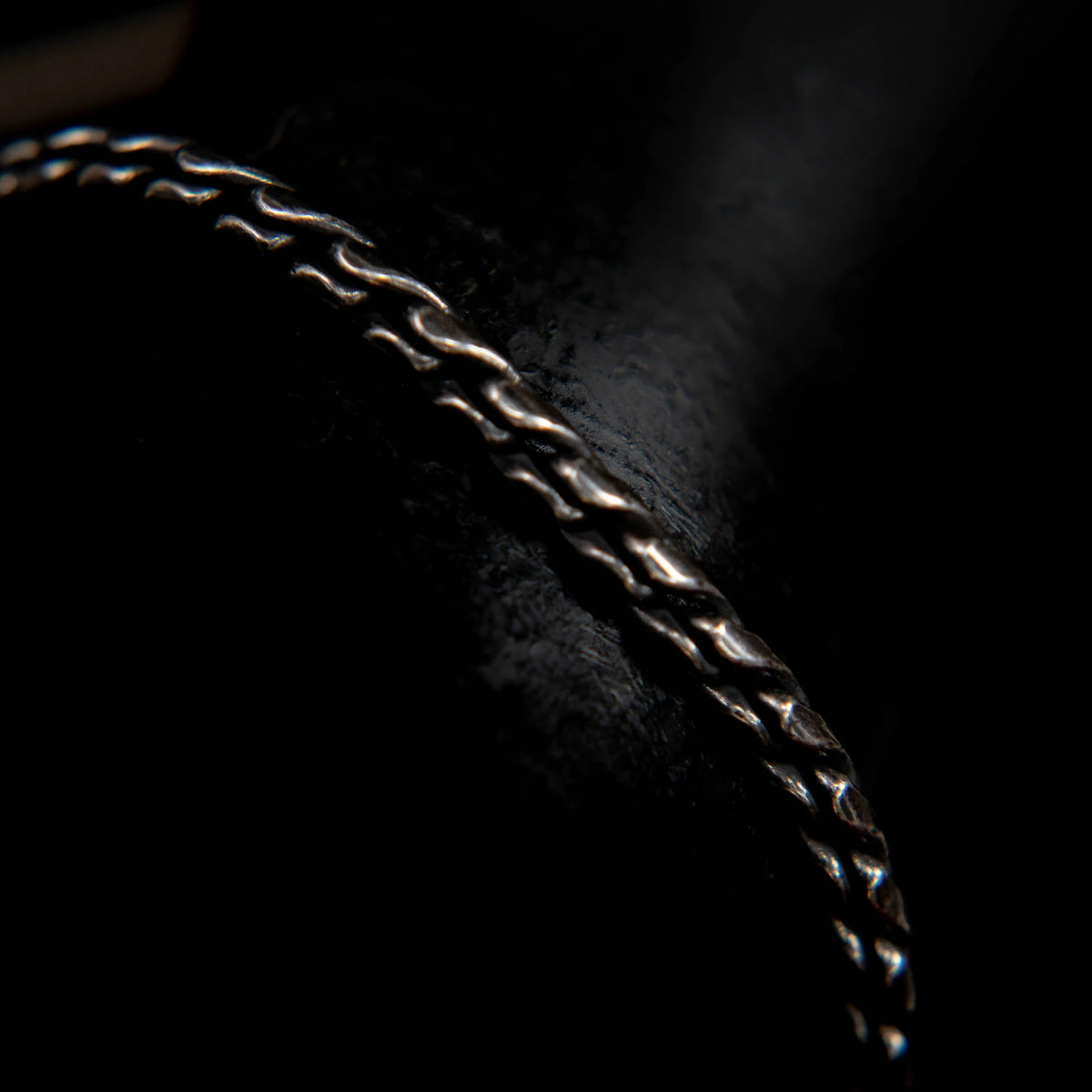 Metallic chain or necklace with interlocking links, partially illuminated against a dark background.