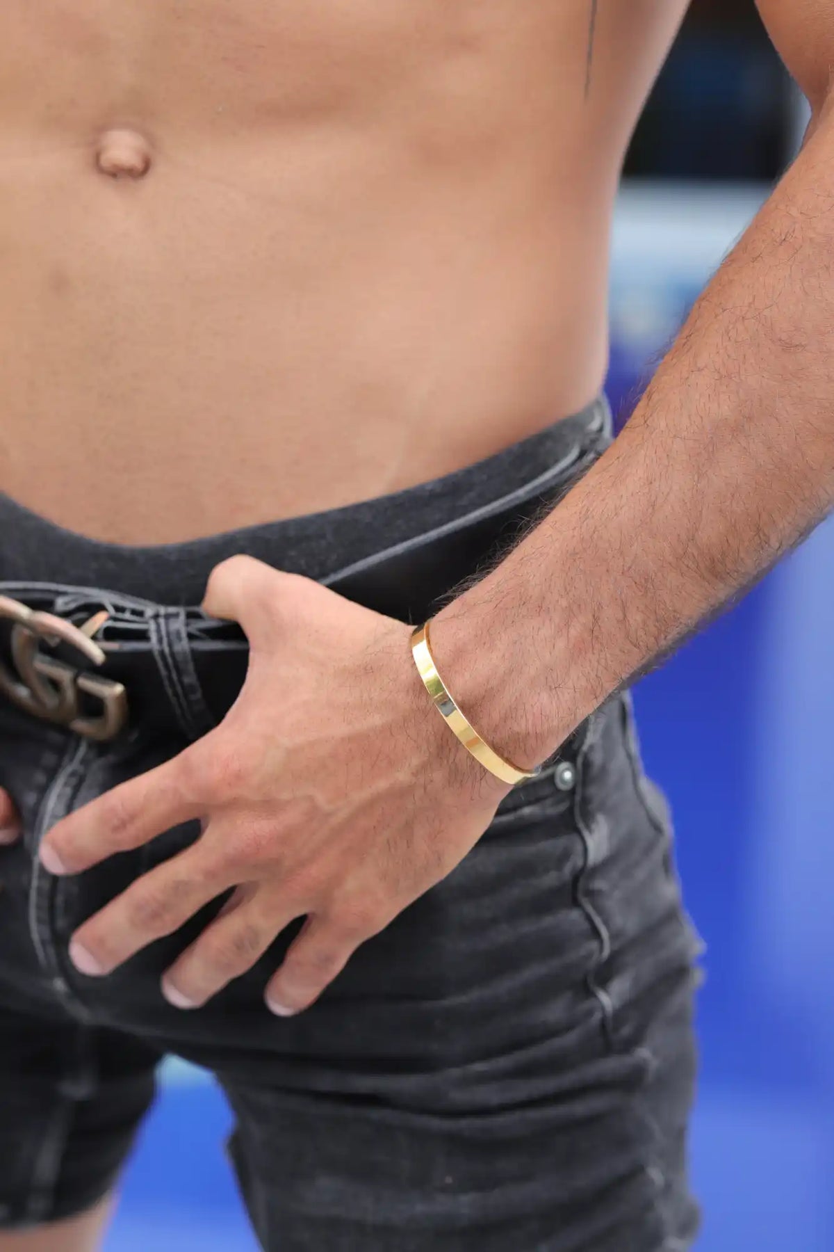 Gold bracelet worn on a wrist alongside dark jeans.