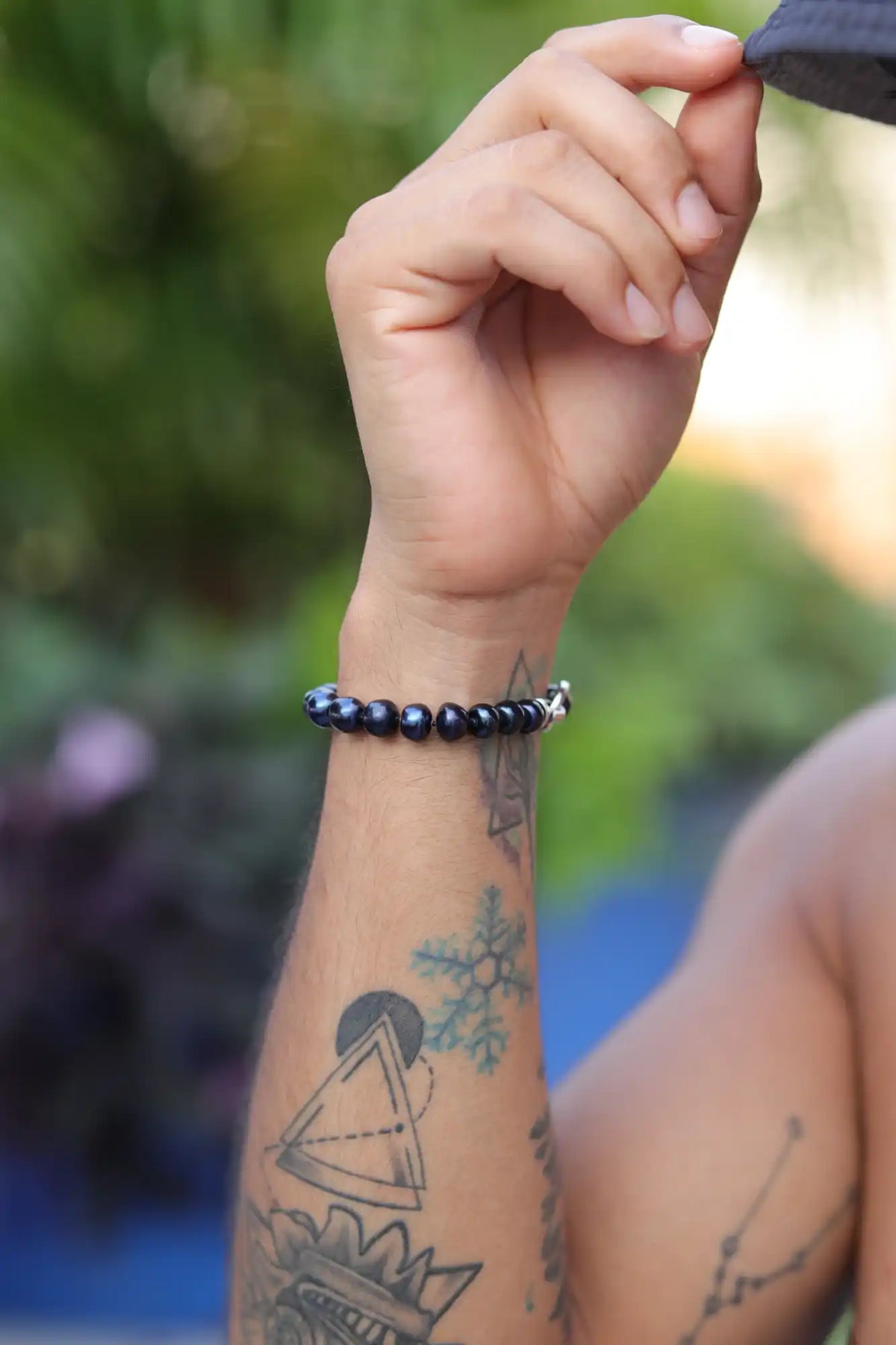 Hand with geometric tattoo art wearing a dark beaded bracelet.