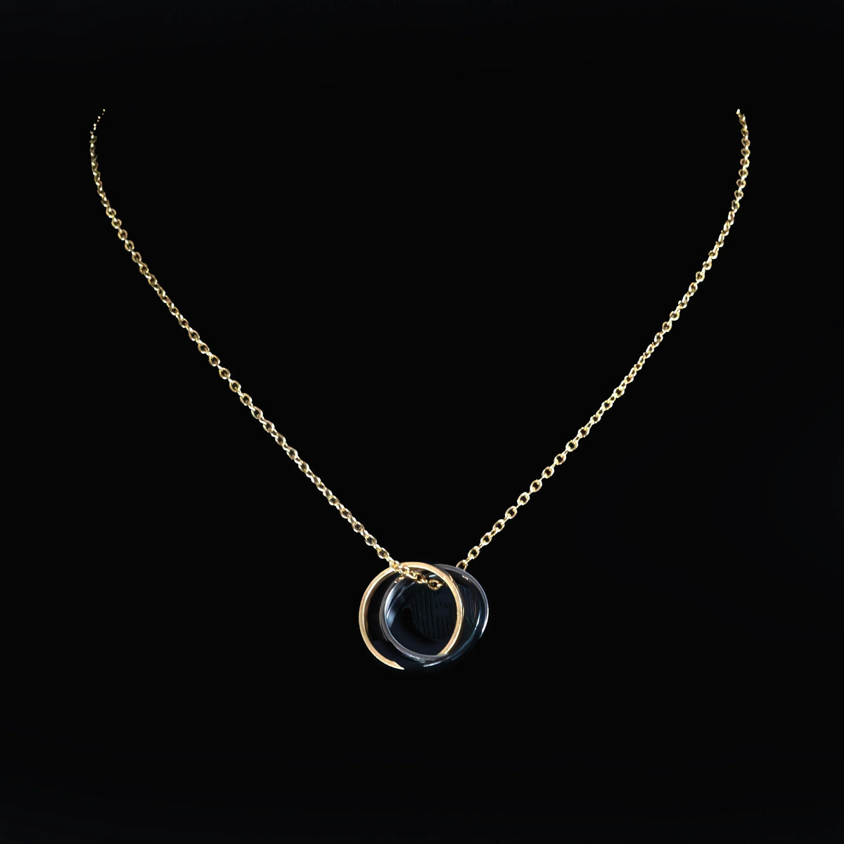 Gold necklace with a circular pendant featuring a dark stone or gem.