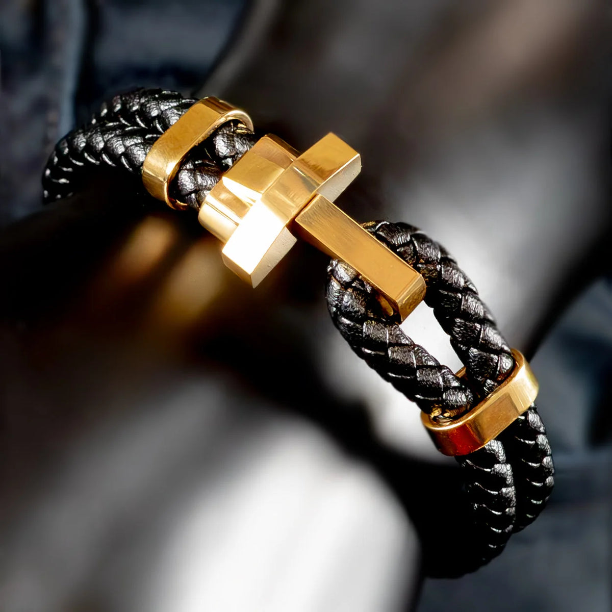 Bracelet with a gold cross charm on a black braided leather band.