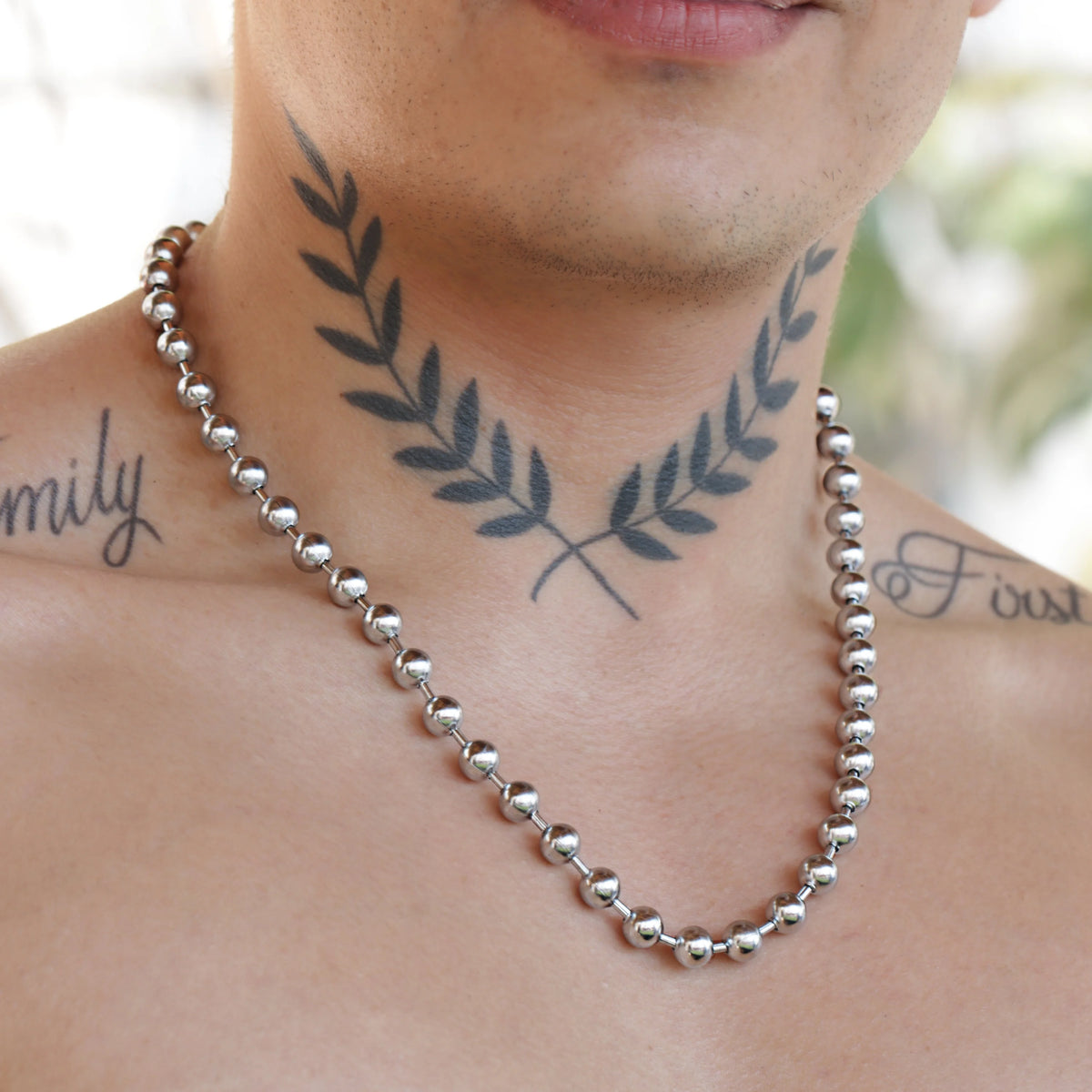 Silver beaded necklace worn with a laurel wreath neck tattoo.