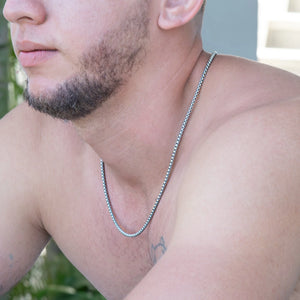 Silver chain necklace worn by a man with facial hair and a visible tattoo on his chest.