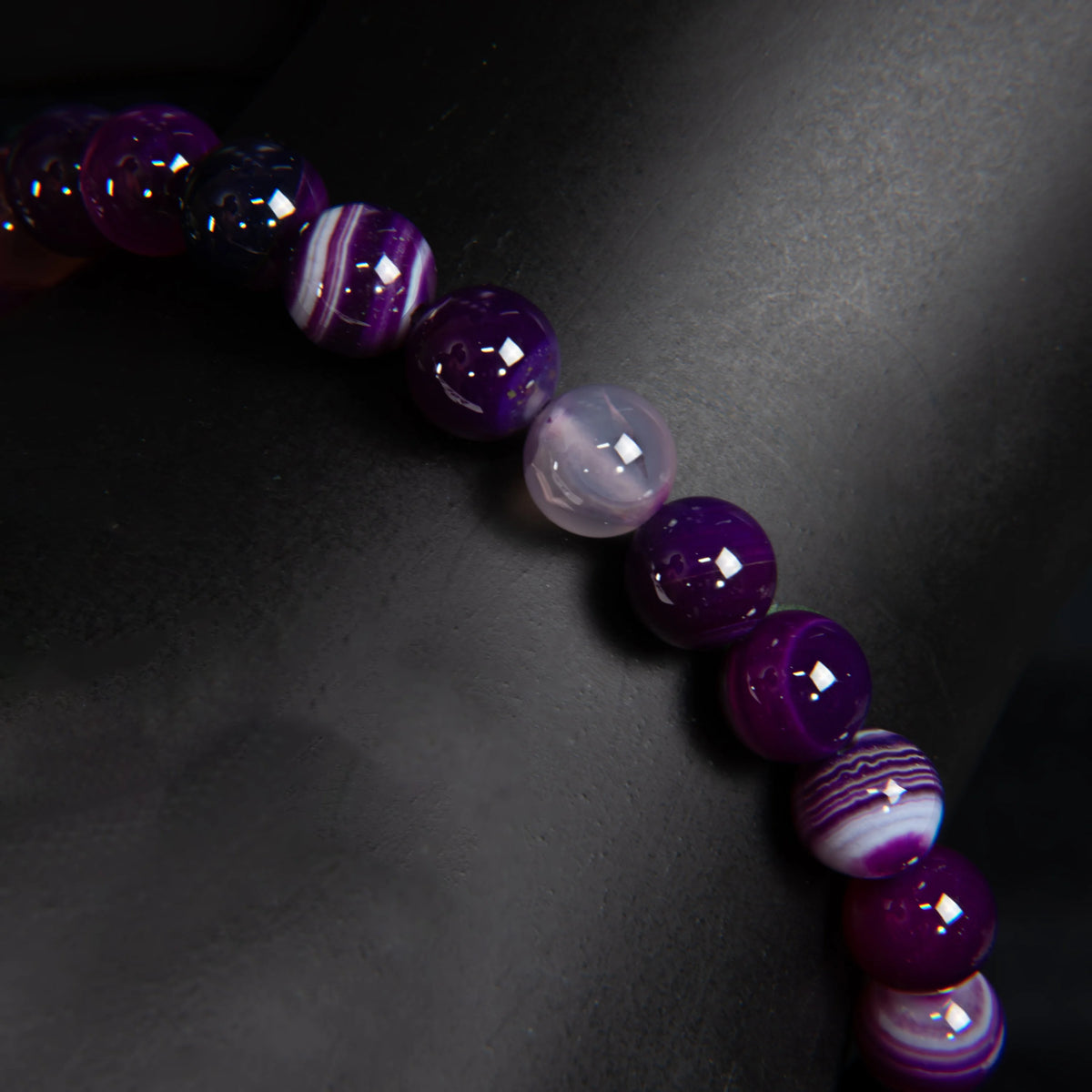 String of purple and lavender gemstone or glass beads with varying patterns and shades.