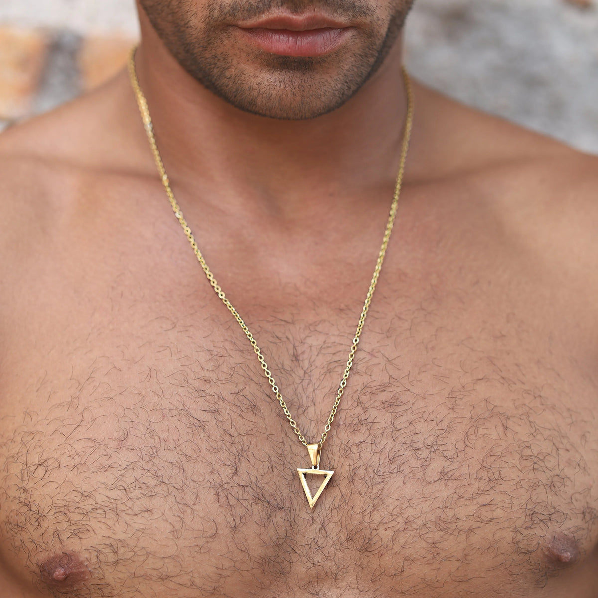 Gold triangle pendant necklace worn on a bare chest.