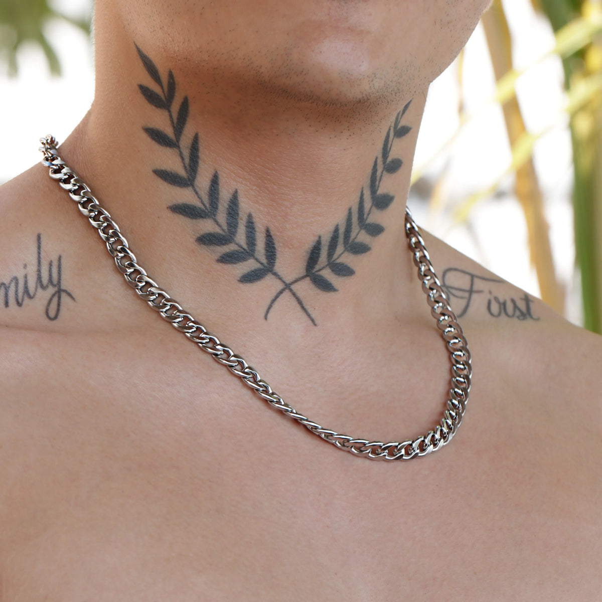 Tattoo of crossed laurel branches on a neck, with a silver chain necklace below.