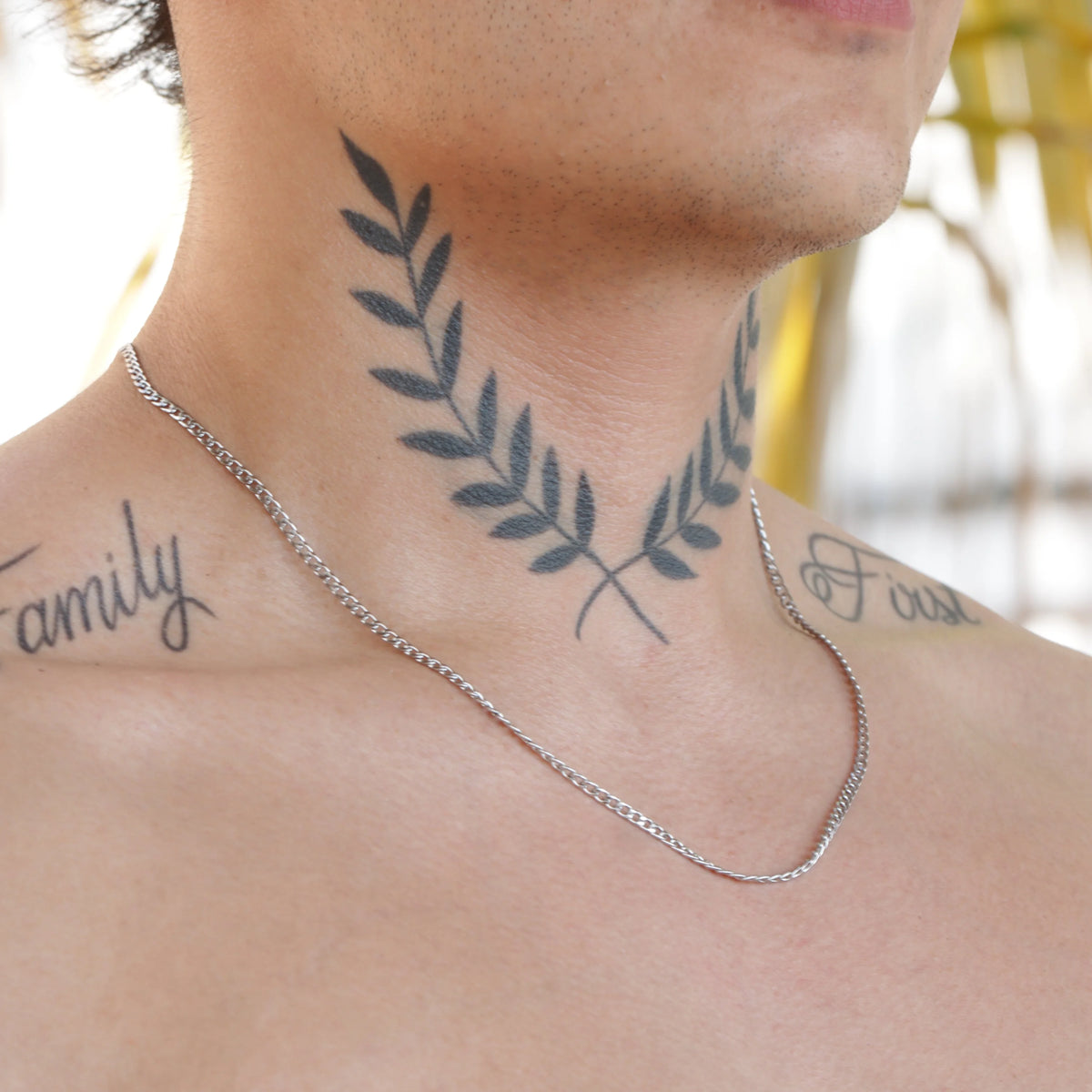 Tattoo of crossed olive branches on a person’s neck.