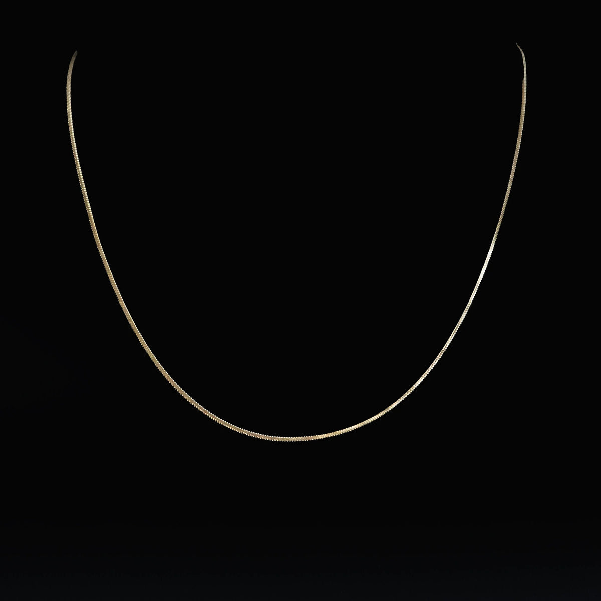 Delicate gold chain necklace against a black background.