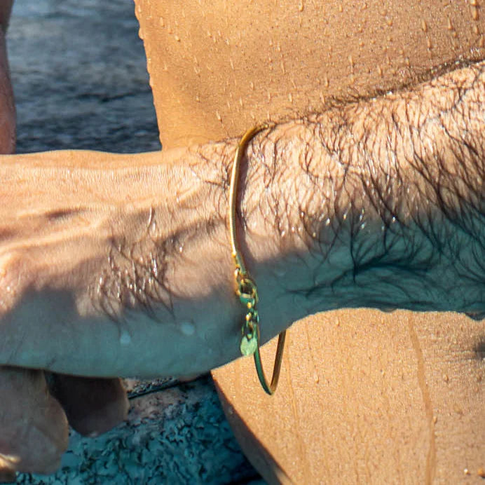 Green and gold bracelet on a tanned arm.