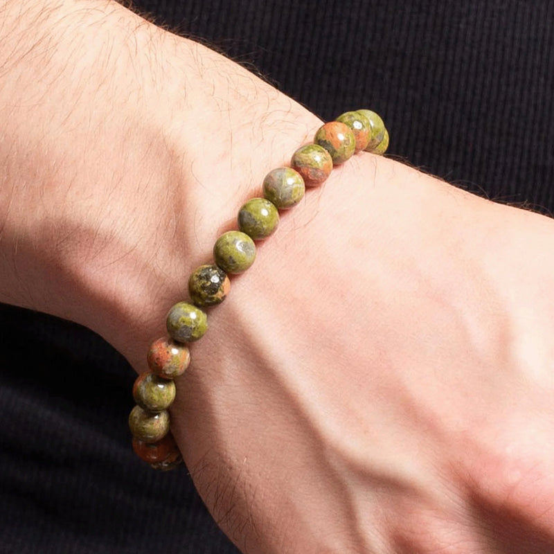 Bracelet made of green and brown stone beads worn on a wrist.