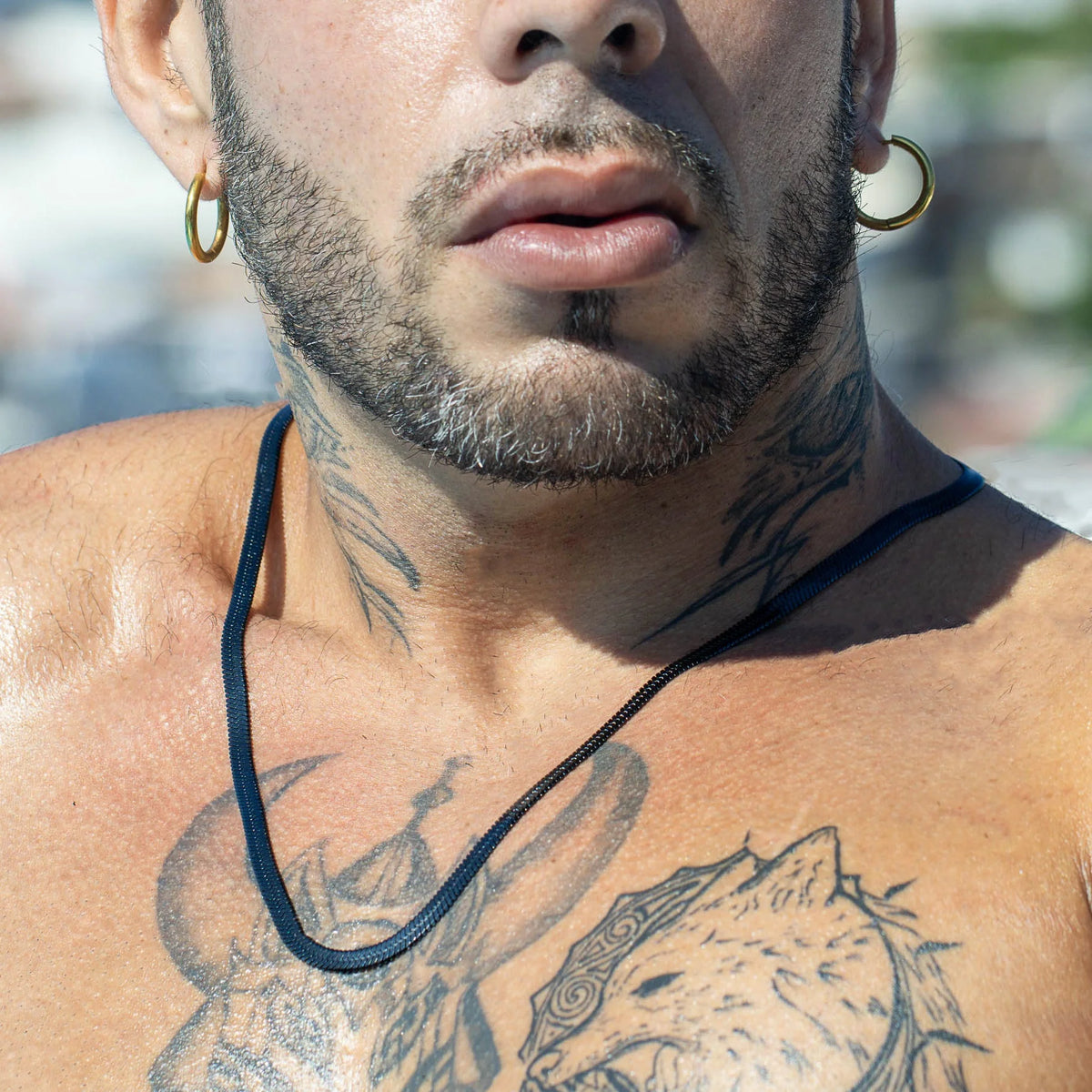 Close-up view of a tattooed chest and neck with gold hoop earrings.