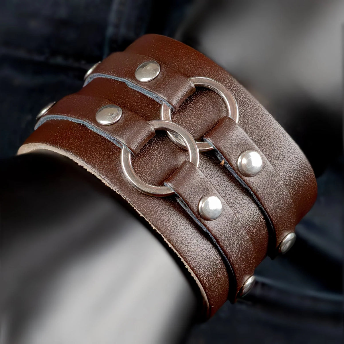 Brown leather cuff bracelet with metal rings and studs.