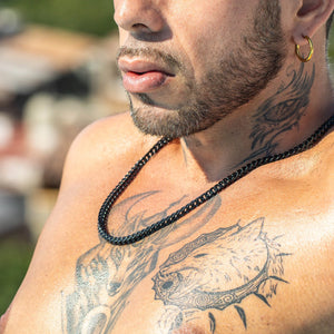 Black beaded chain necklace worn against tattooed skin.