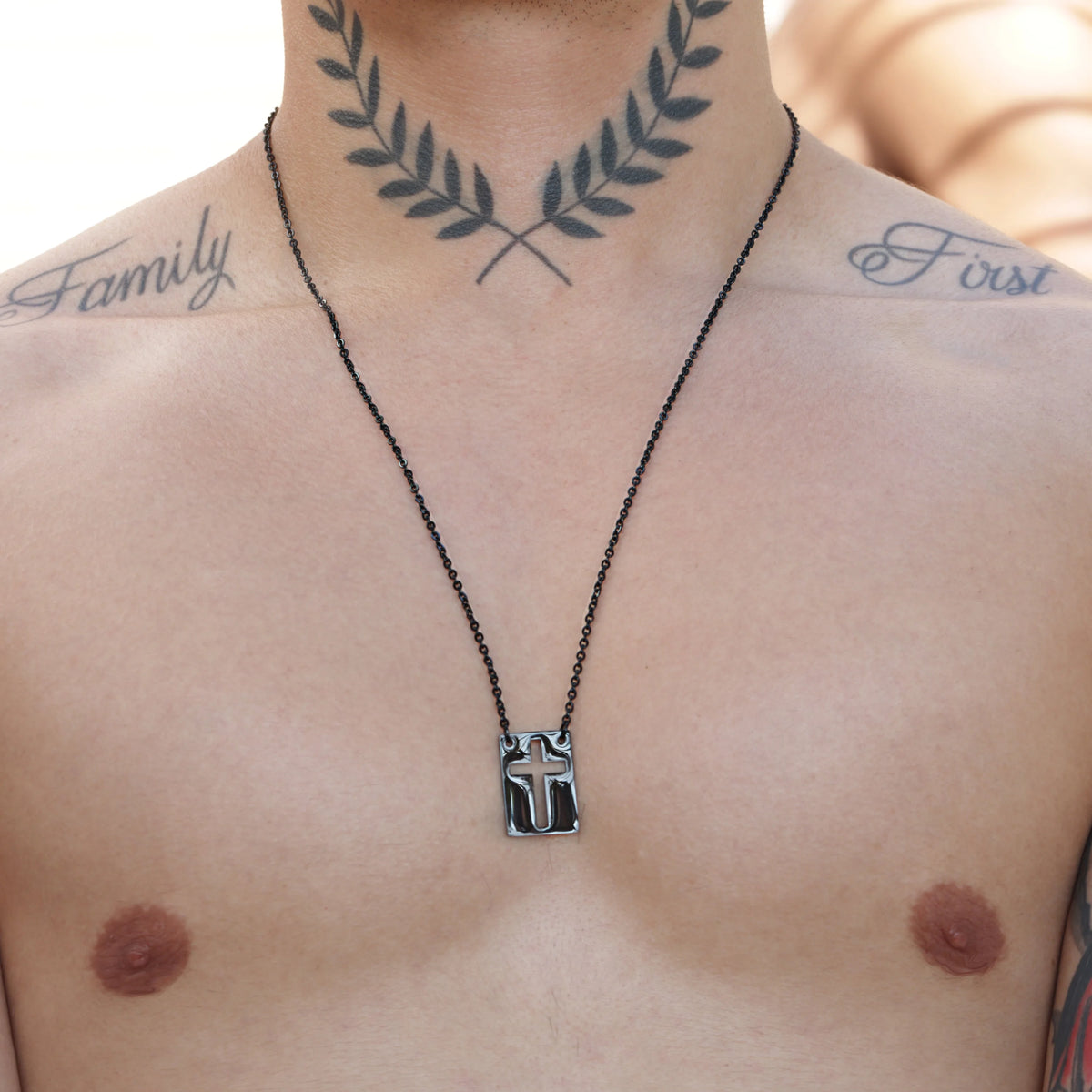 Necklace with a small pendant hanging on a bare chest with tattoos visible.