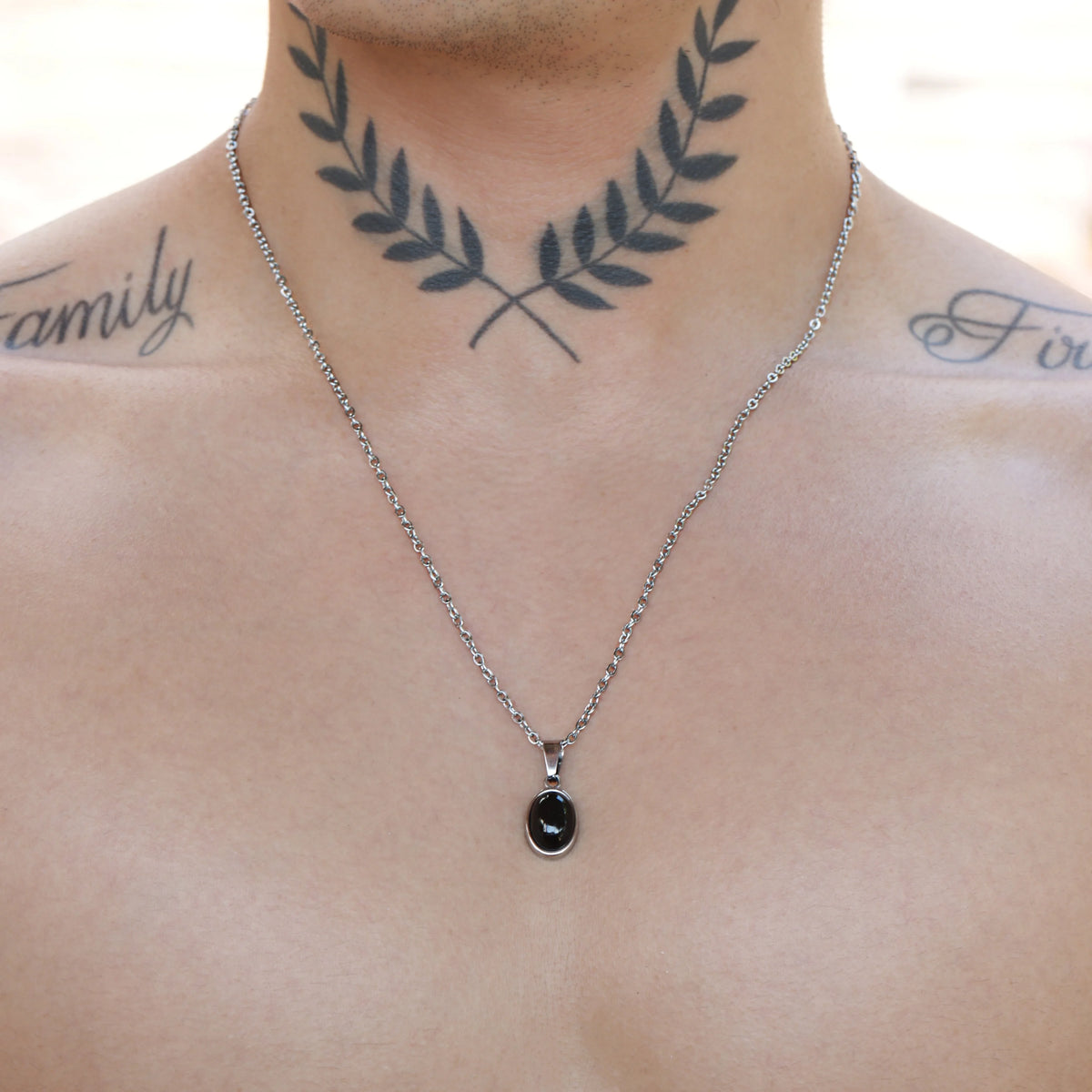 Tattoo of crossed laurel branches on a person’s neck, with a necklace below it.