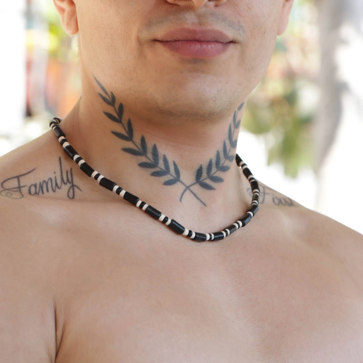 Black and white beaded necklace worn with a laurel branch neck tattoo.