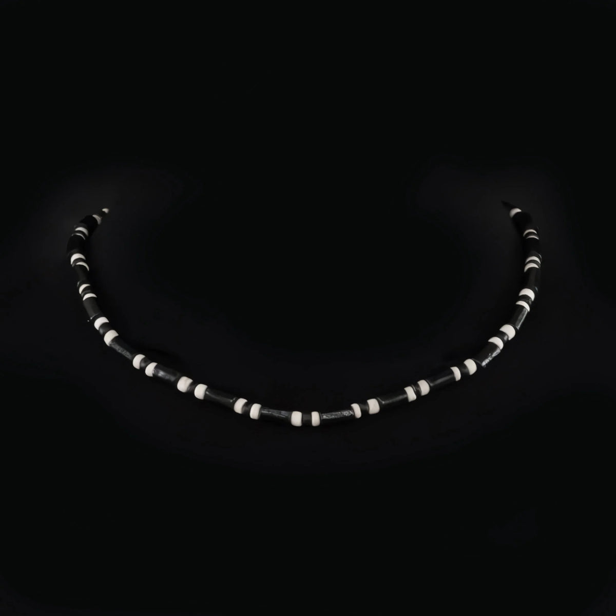 Curved string of alternating black and white beads against a dark background.