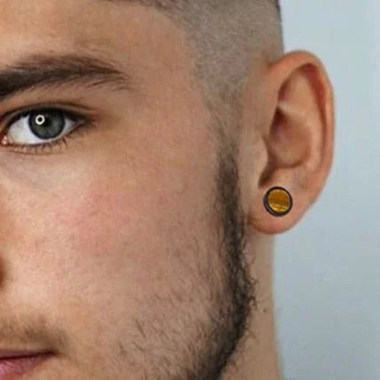 Close-up view of a person’s face showing an eye, partial beard, and ear with a yellow-amber gauge earring.